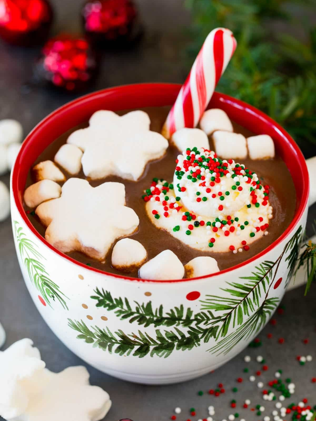 A steaming mug of hot cocoa with a cinnamon stick and whipped cream.
