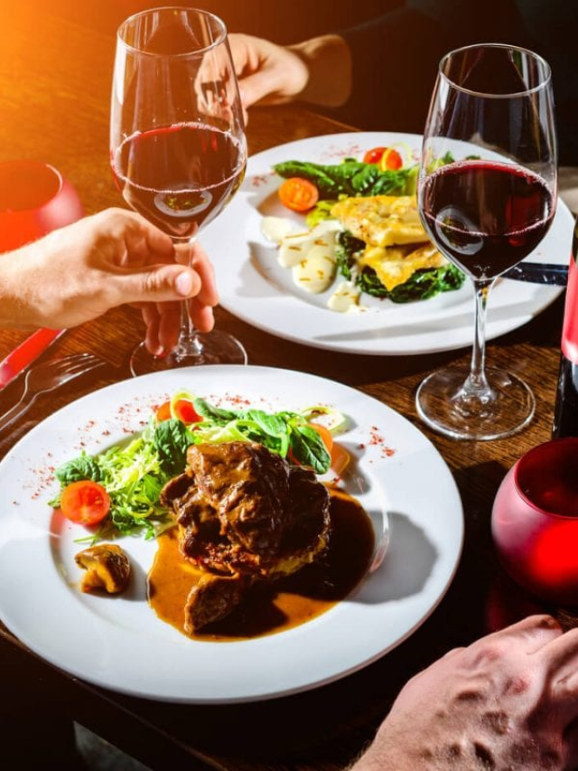 A beautifully set dinner table with a plate of steak, sides, and wine glasses.
