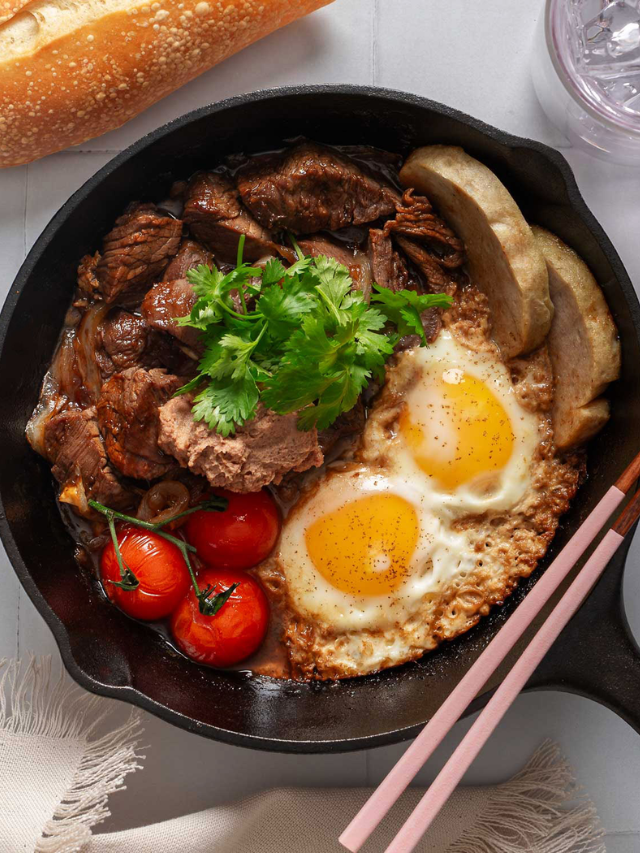 A sizzling steak in a pan with butter splattering around it.
