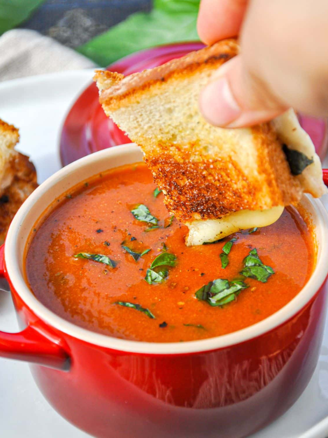 A steaming bowl of creamy tomato soup with a grilled cheese sandwich on the side.
