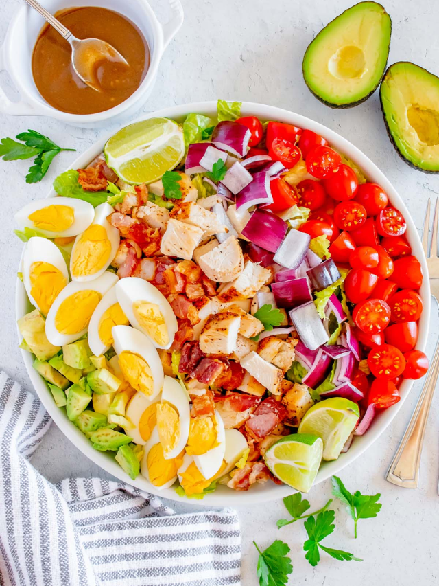 A close-up of a chopped salad with grilled chicken, avocado, crumbled cheese, and a balsamic vinaigrette
