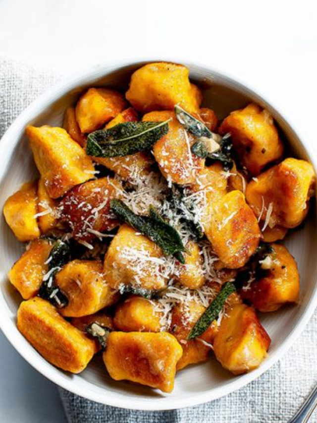 A plate of pillowy gnocchi bathed in a creamy pumpkin sauce, topped with sage leaves.
