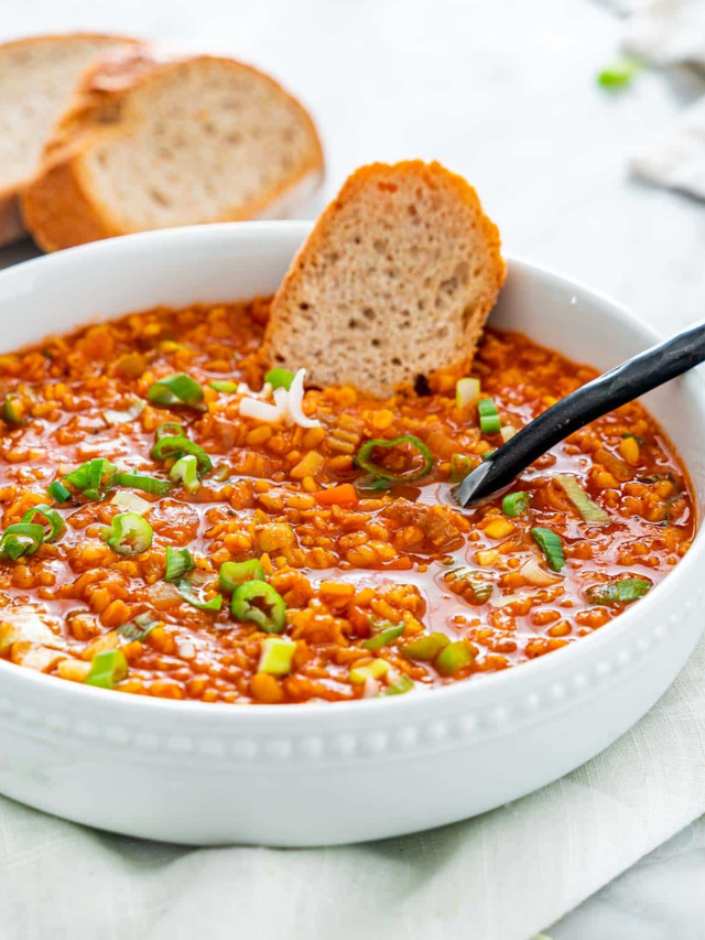 A steaming bowl of lentil soup with crusty bread on the side.
