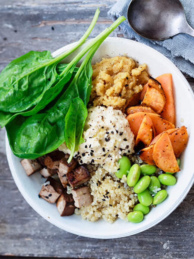 A colorful Buddha bowl filled with quinoa, roasted vegetables, chickpeas, avocado, and a tahini dressing.
