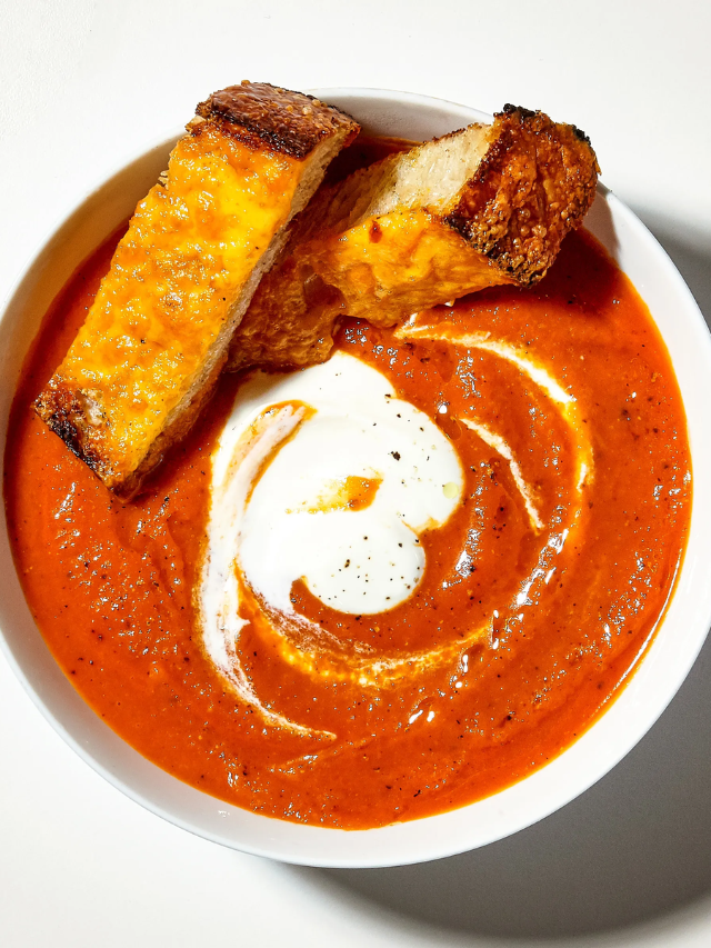  A steaming mug of tomato soup next to a colorful side salad.
