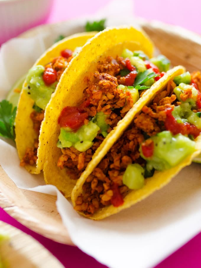 A colorful platter filled with hard and soft taco shells, seasoned ground beef, shredded cheese, lettuce, tomatoes, and various toppings.

