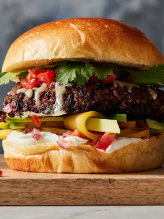 A close-up of a portobello mushroom burger on a whole wheat bun with lettuce, tomato, and vegan cheese.
