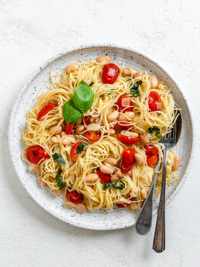 A pot of creamy pasta with white beans, kale, and cherry tomatoes.
