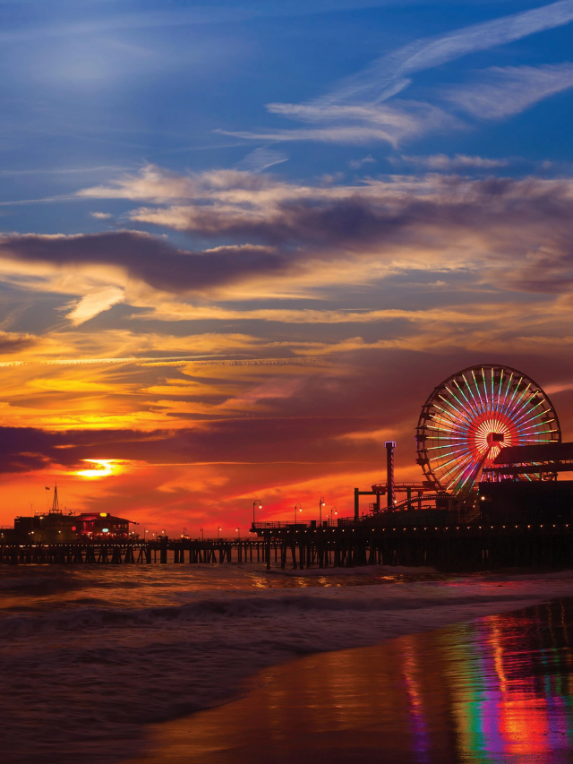A sunset over the Santa Monica Pier, casting a warm glow on the ocean and palm trees.

