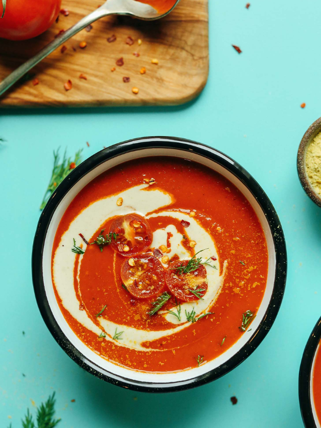 A steaming bowl of creamy tomato soup with a grilled cheese sandwich on the side.
