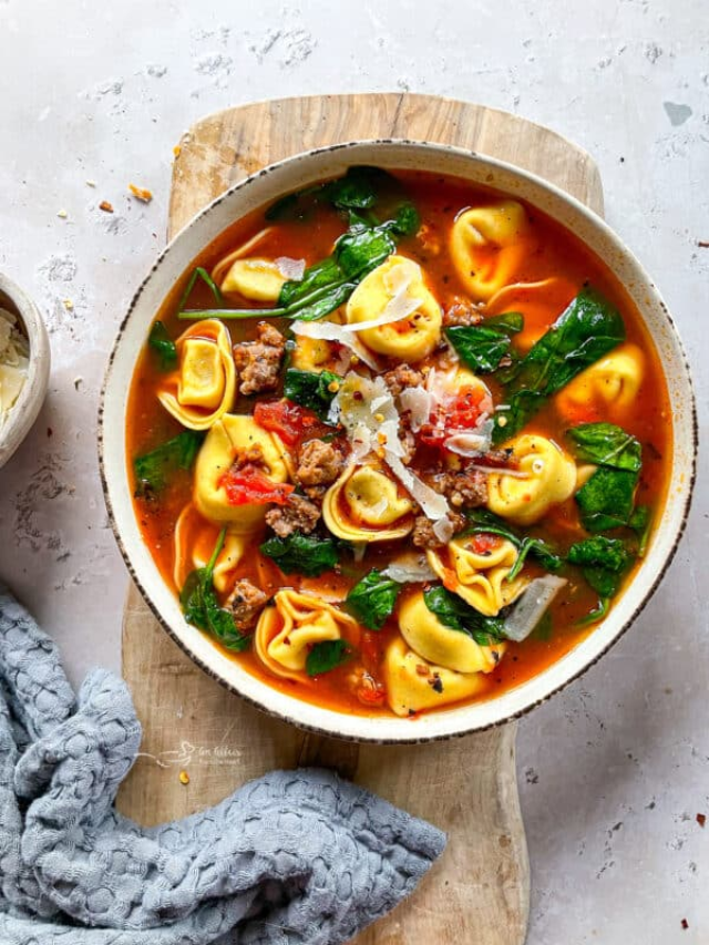 A pot filled with creamy tomato tortellini soup garnished with fresh basil.
