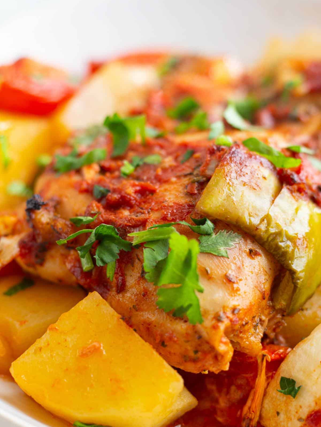 A sheet pan with chicken breasts, potatoes, and colorful vegetables.
