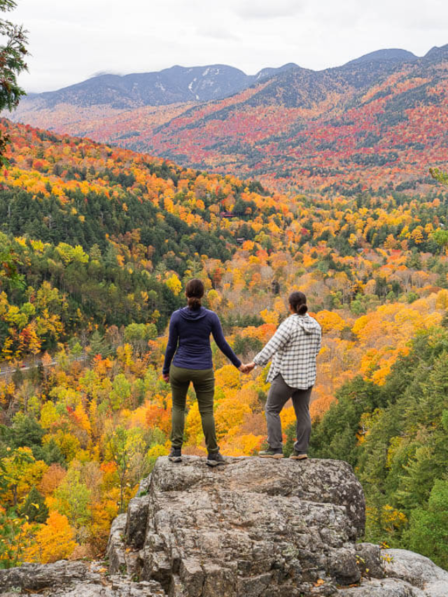 Hiker standing on a scenic trail overlooking a lush forest with a glimpse of the lake below.
