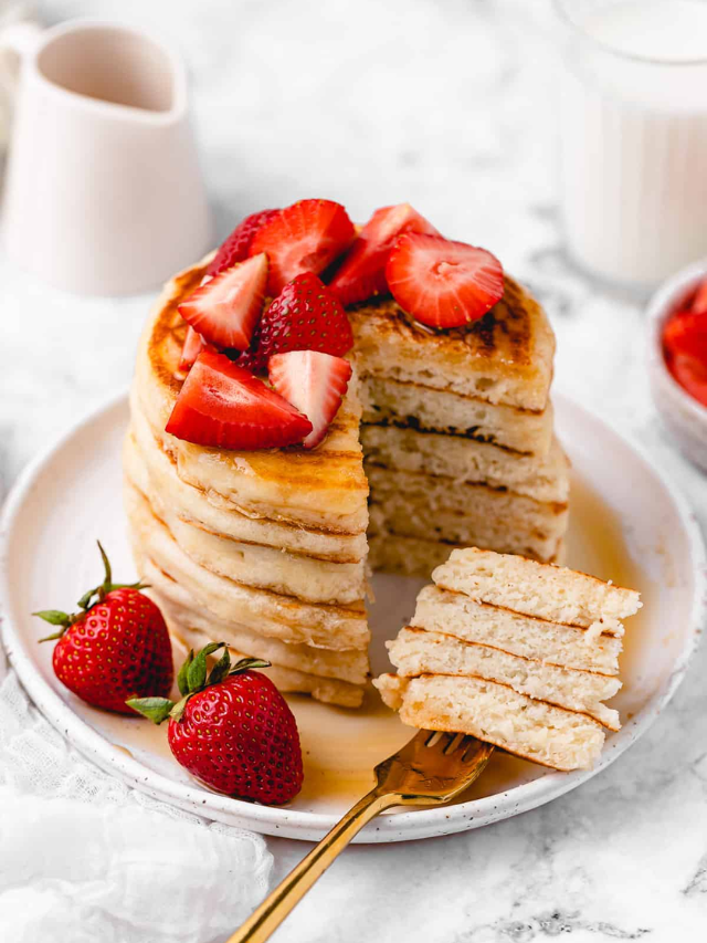 A stack of fluffy pancakes with berries and whipped cream.

