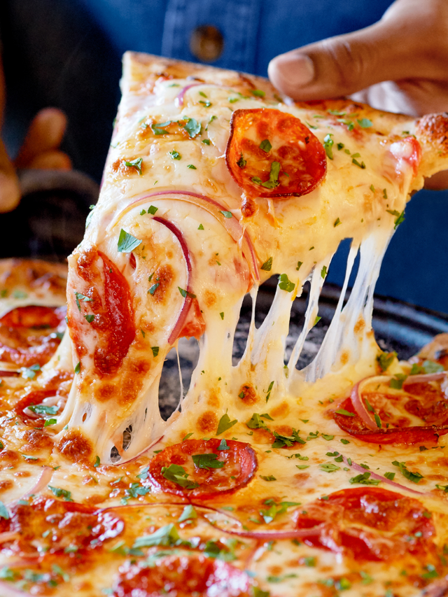 A thin-crust pizza with melted cheese, vegetables, and sausage being grilled
