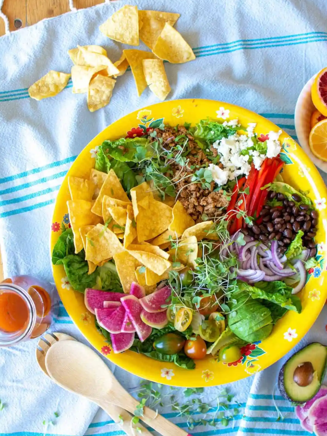 A colorful taco salad bowl with ground beef, lettuce, tomatoes, cheese, and tortilla chips.
