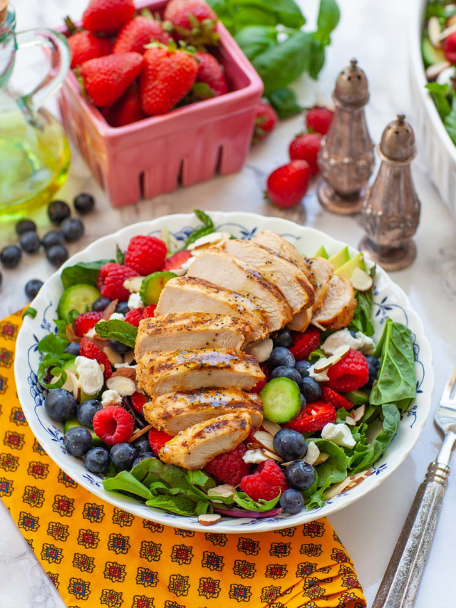 A colorful salad with grilled chicken, mixed greens, cherry tomatoes, cucumbers, feta cheese, and a balsamic vinaigrette.
