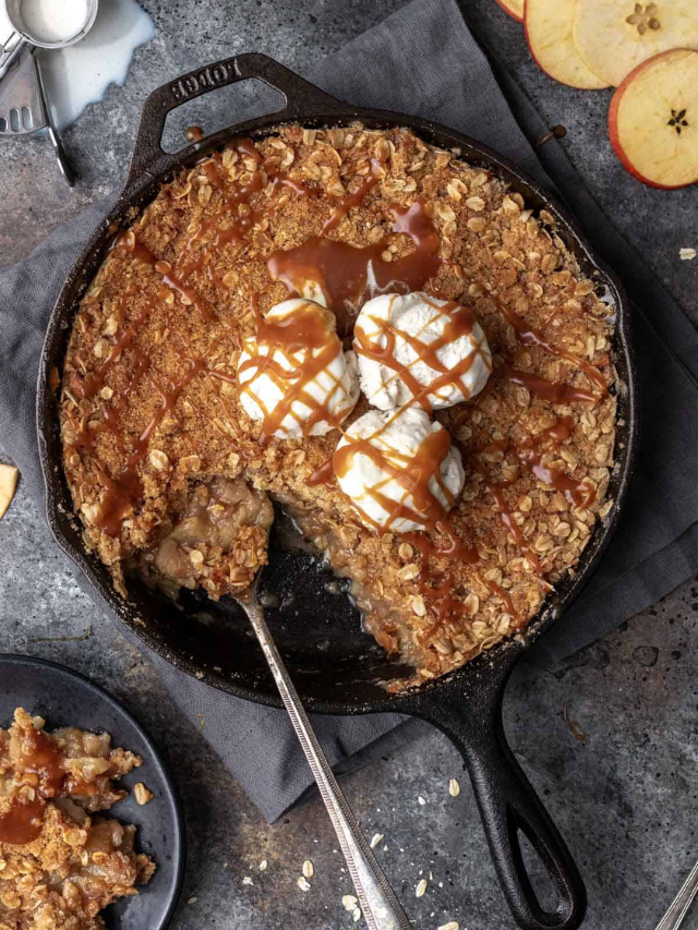 A photo of an apple crisp casserole with a golden brown oat topping and a scoop of vanilla ice cream on the side.
