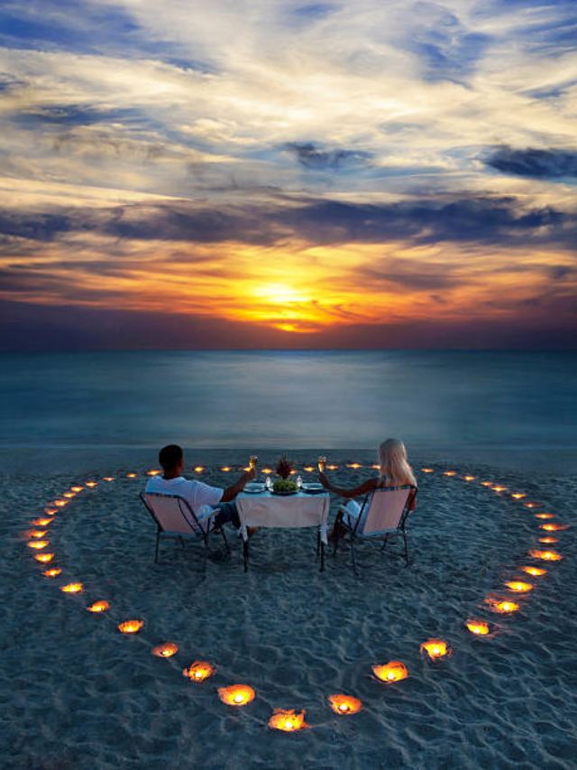  A couple enjoying a romantic sunset dinner on a secluded beach, with tiki torches illuminating the scene.
