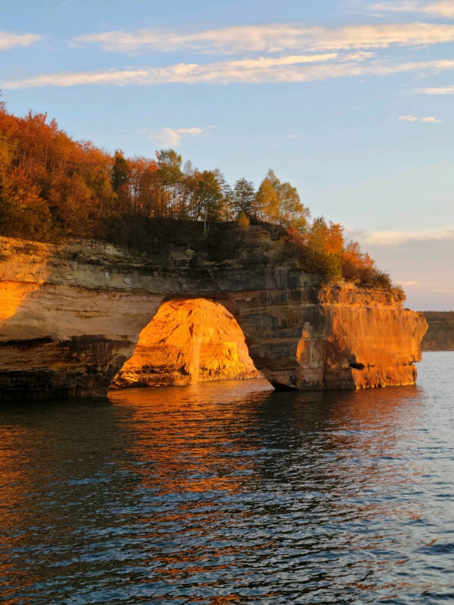 Majestic sandstone cliffs along the shore of Lake Superior with colorful mineral formations and waterfalls cascading down the rocks.
