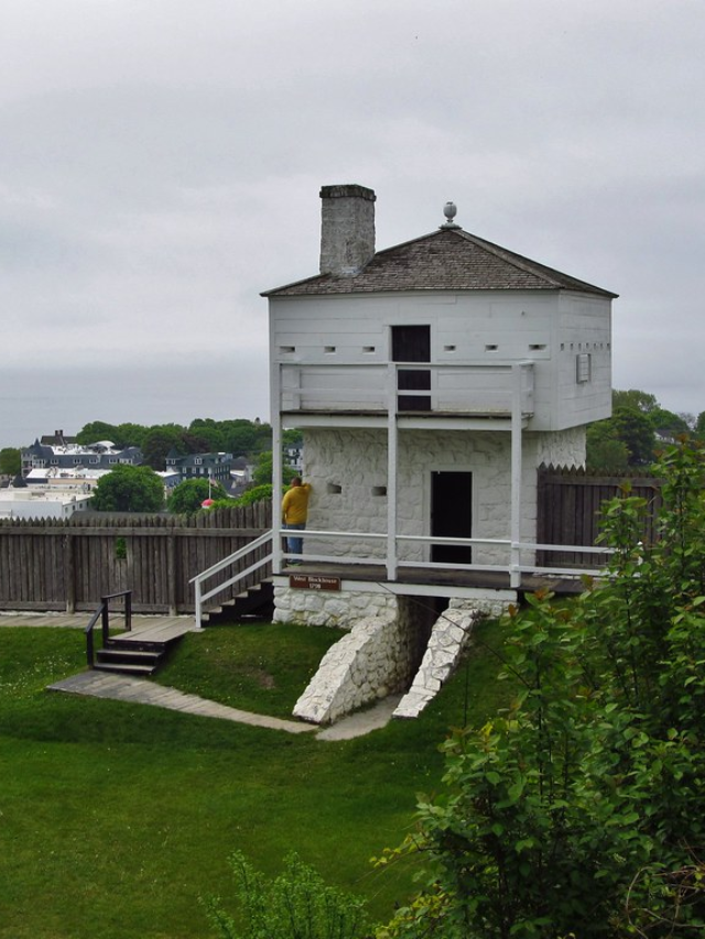 Fort Mackinac, a star-shaped fort overlooking the water, with cannons and soldiers in period dress.
