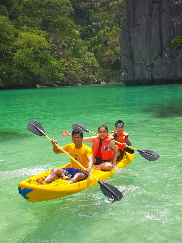 Kayakers paddling on calm turquoise waters with limestone cliffs in the background.
